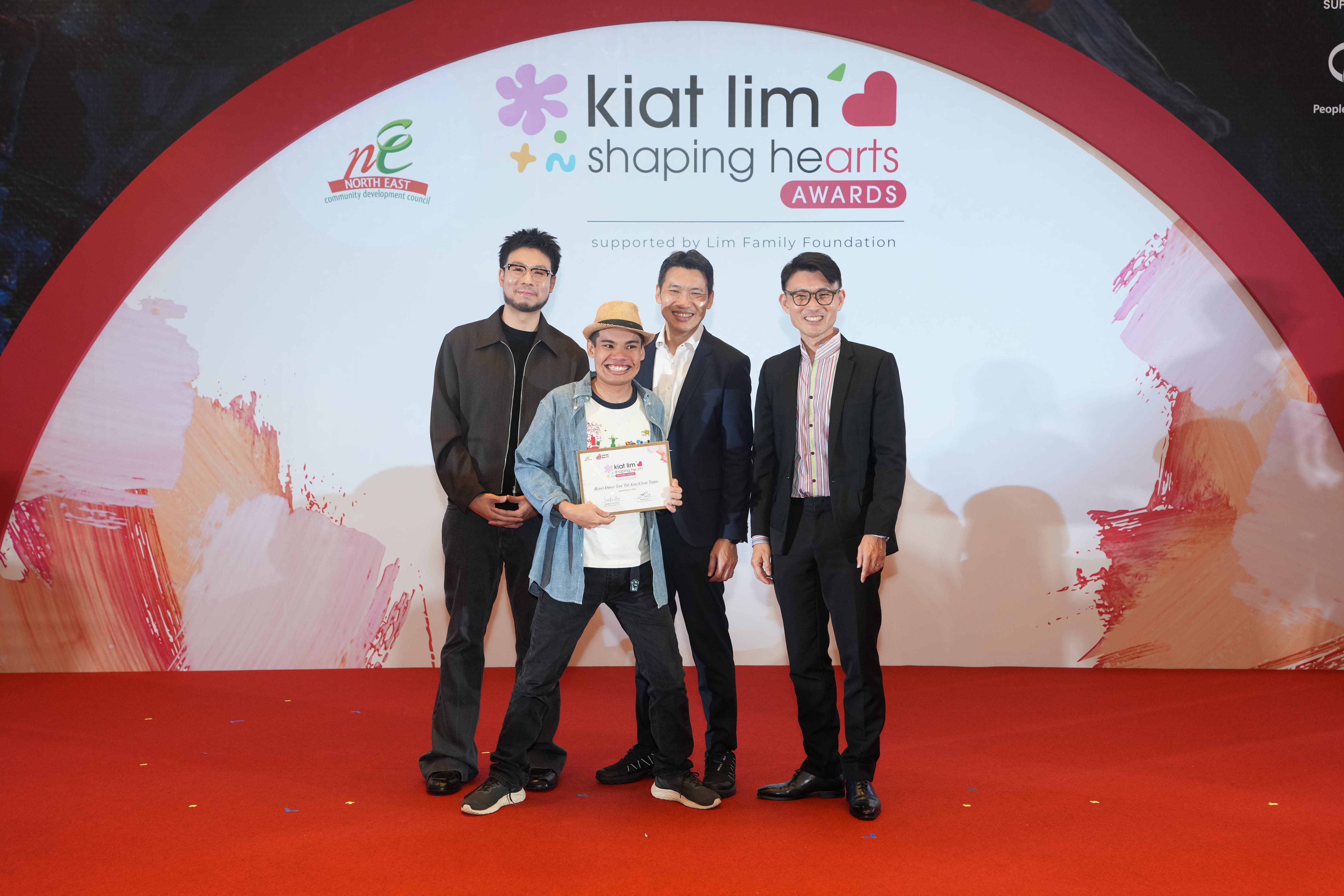 Award recipient standing on stage with the presenter, holding their certificate and posing for a group photo during the award ceremony, with a backdrop reading ‘Kiat Lim-Shaping Hearts Awards'.